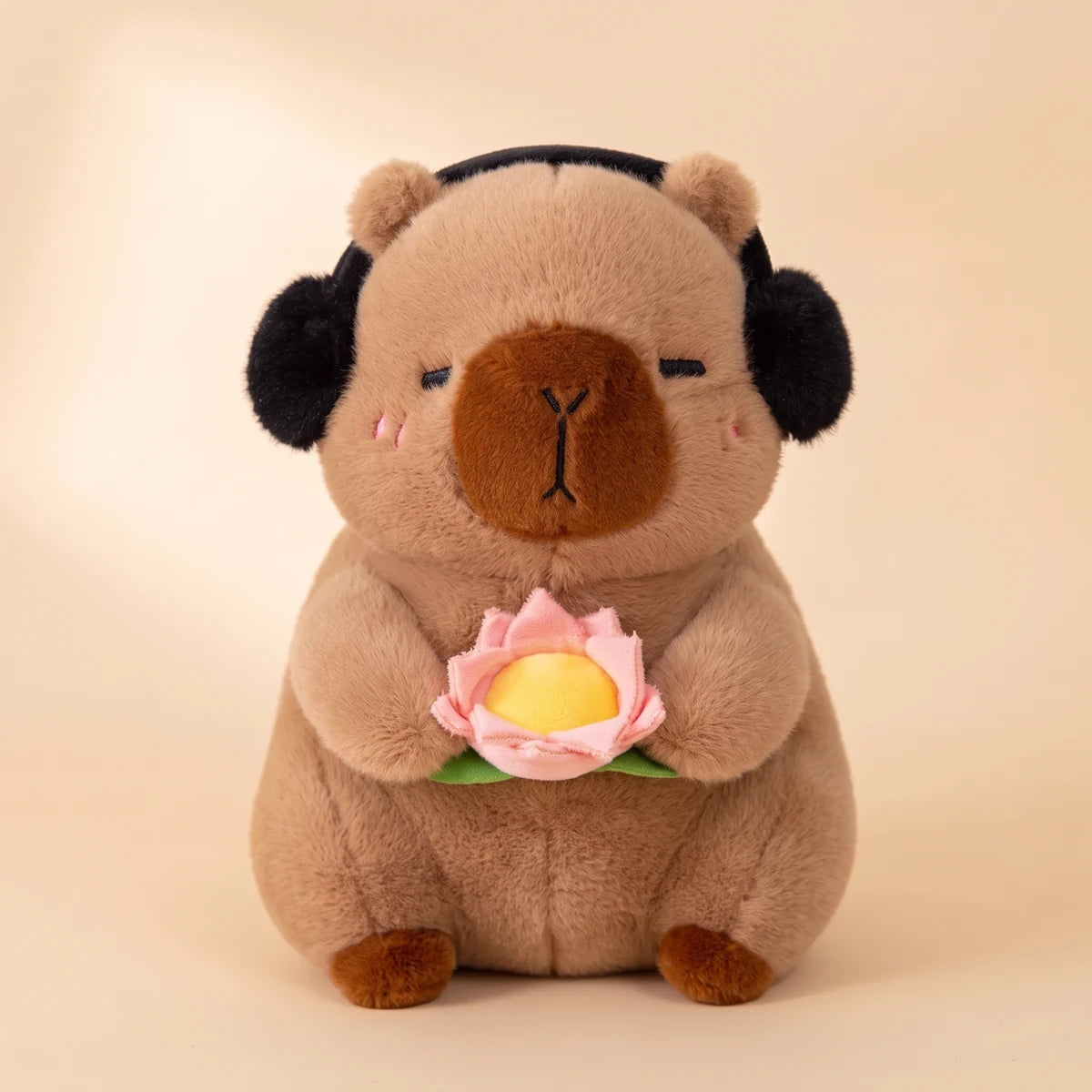 Front view of the brown capybara plush with black headphones holding a pink lotus flower
