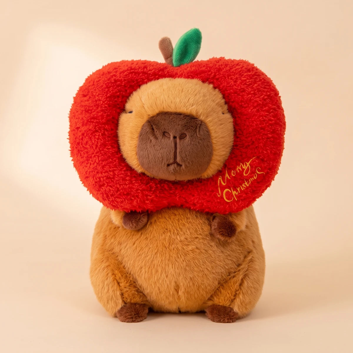 Front view of the capybara plush wearing a red apple hood with a green leaf