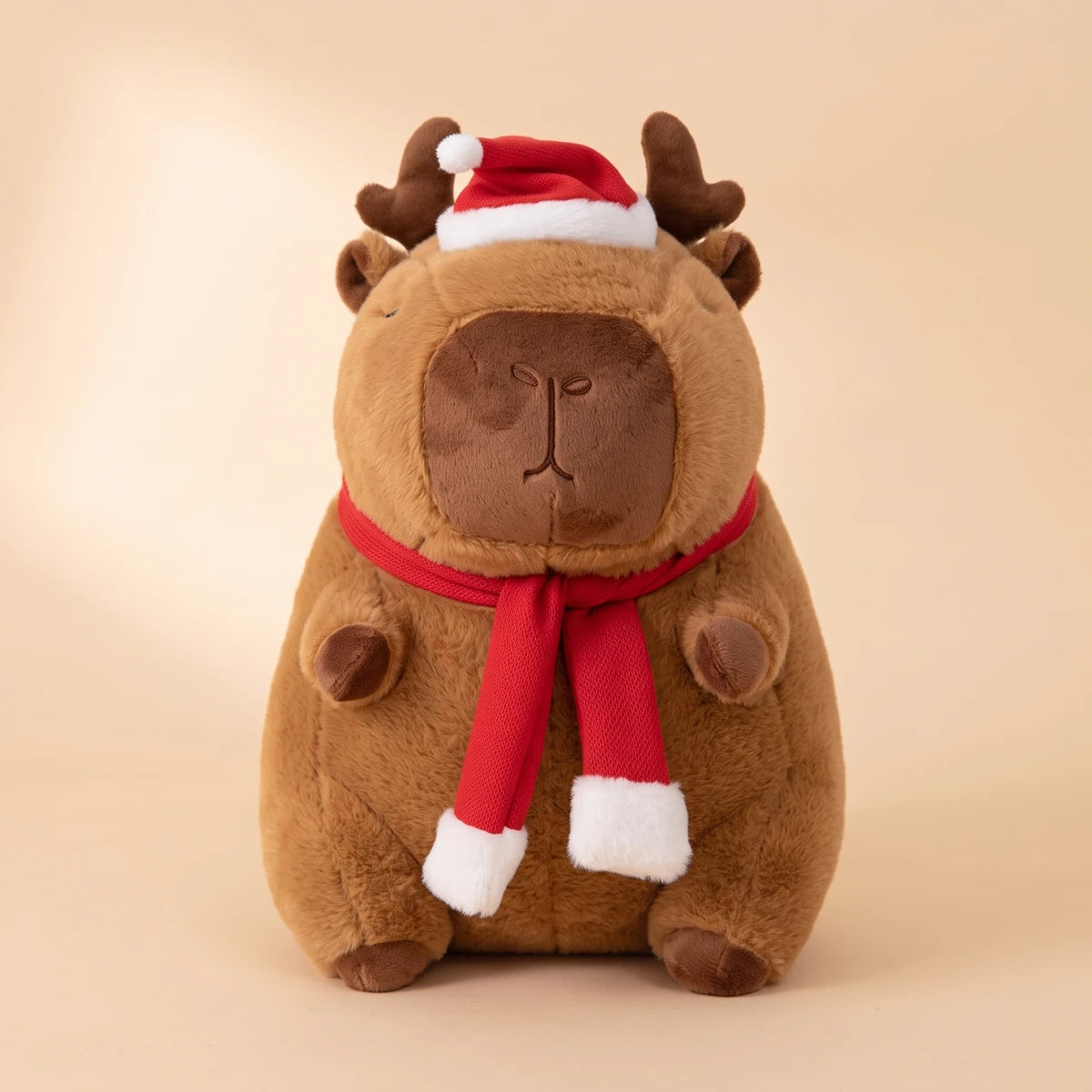 Front view of the reindeer capybara plush with antlers, a Santa hat and a red scarf