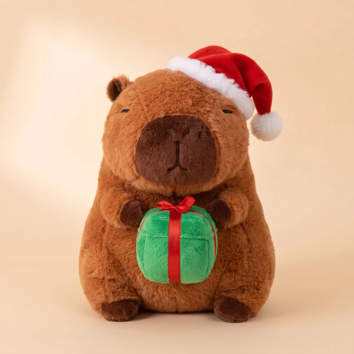 Front view of the Christmas capybara plush wearing a Santa hat and holding a green gift box