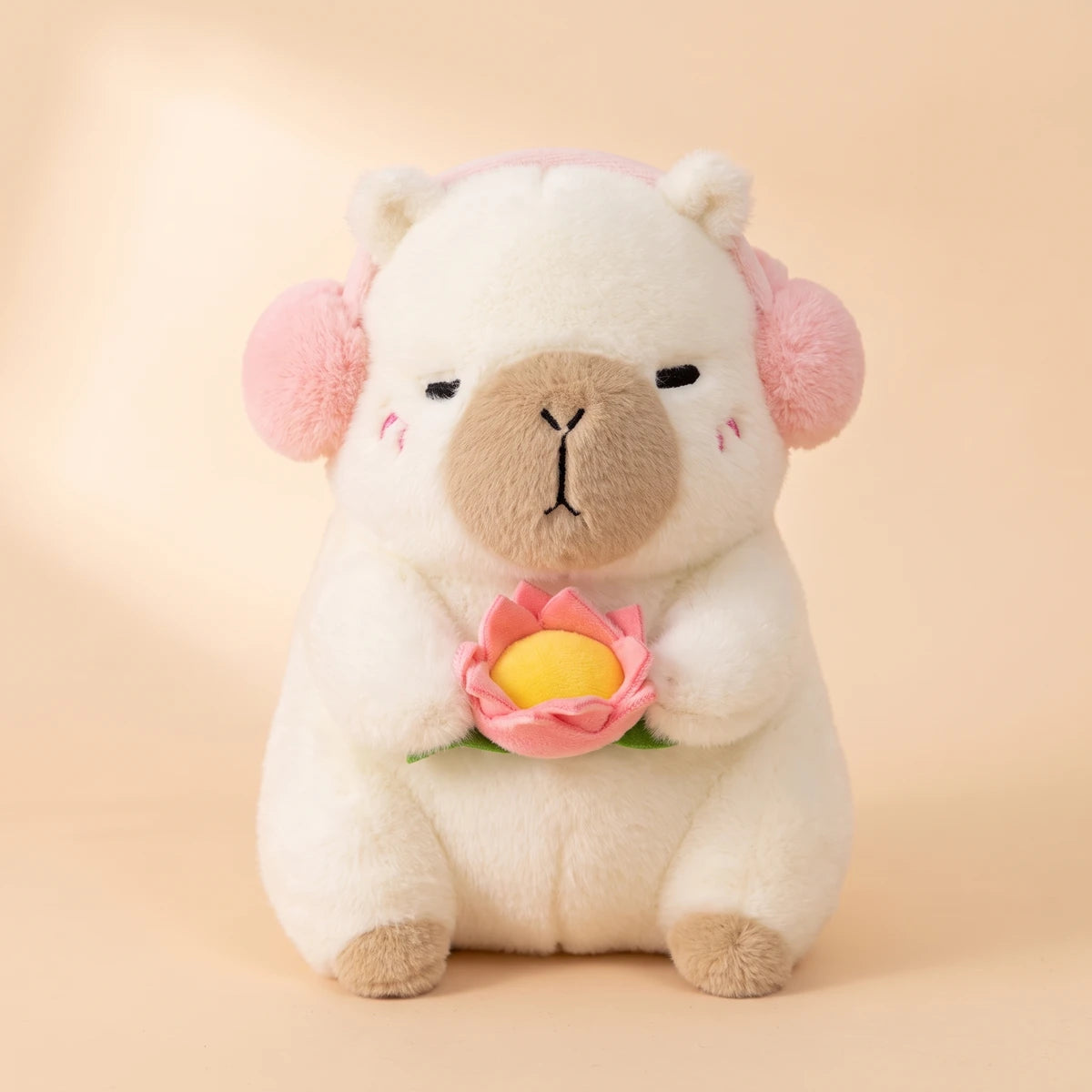 Front view of the white capybara plush with pink headphones holding a pink lotus flower