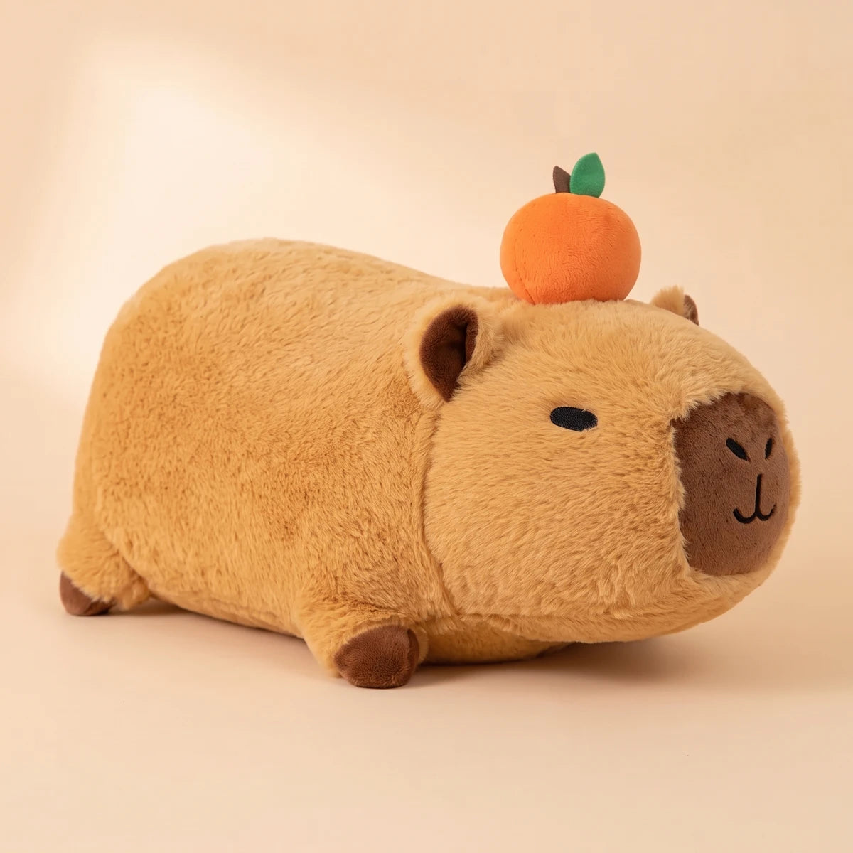Side view of the lying capybara plush with an orange on its head