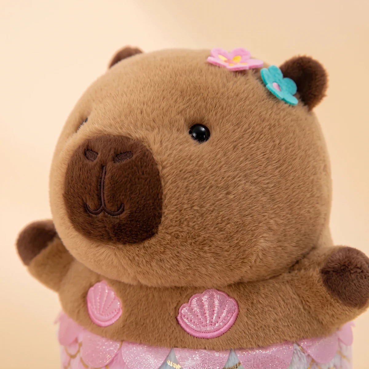 Close-up of the mermaid capybara plush face with two flowers by the ear and pink shells