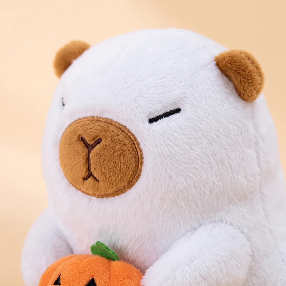 Close-up of the white ghost capybara plush face with caramel ears and muzzle