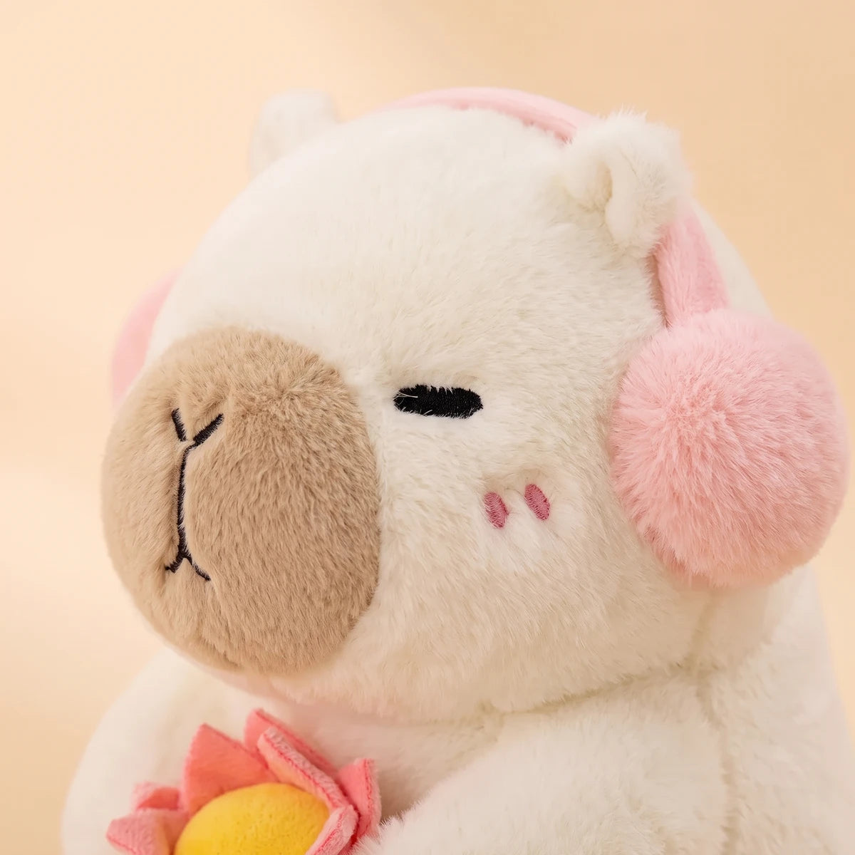 Close-up of the white capybara plush face with fluffy pink headphones