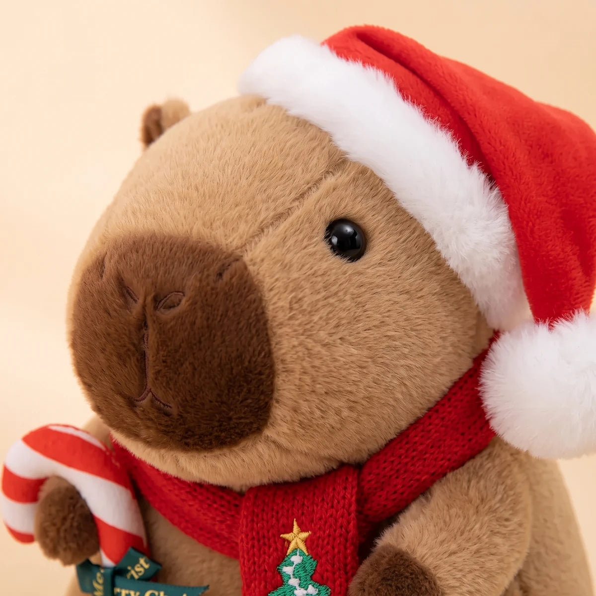 Close-up of the face of the Christmas capybara plush with a Santa hat holding a candy cane