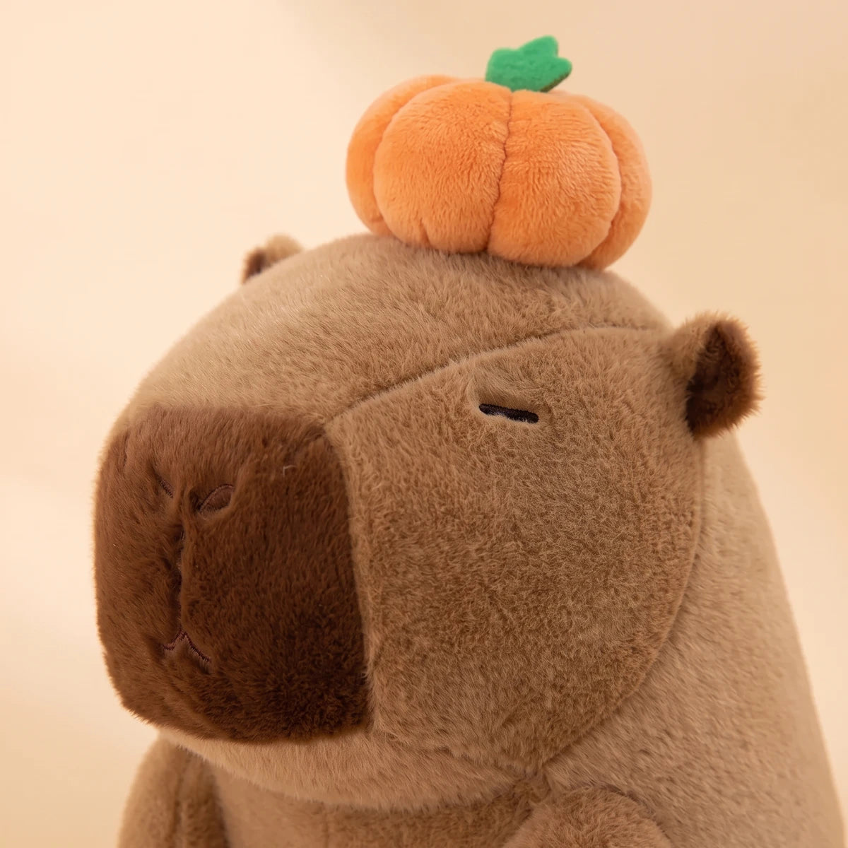 Close-up of the capybara with pumpkin on head plush showing its stitched eye and small pumpkin