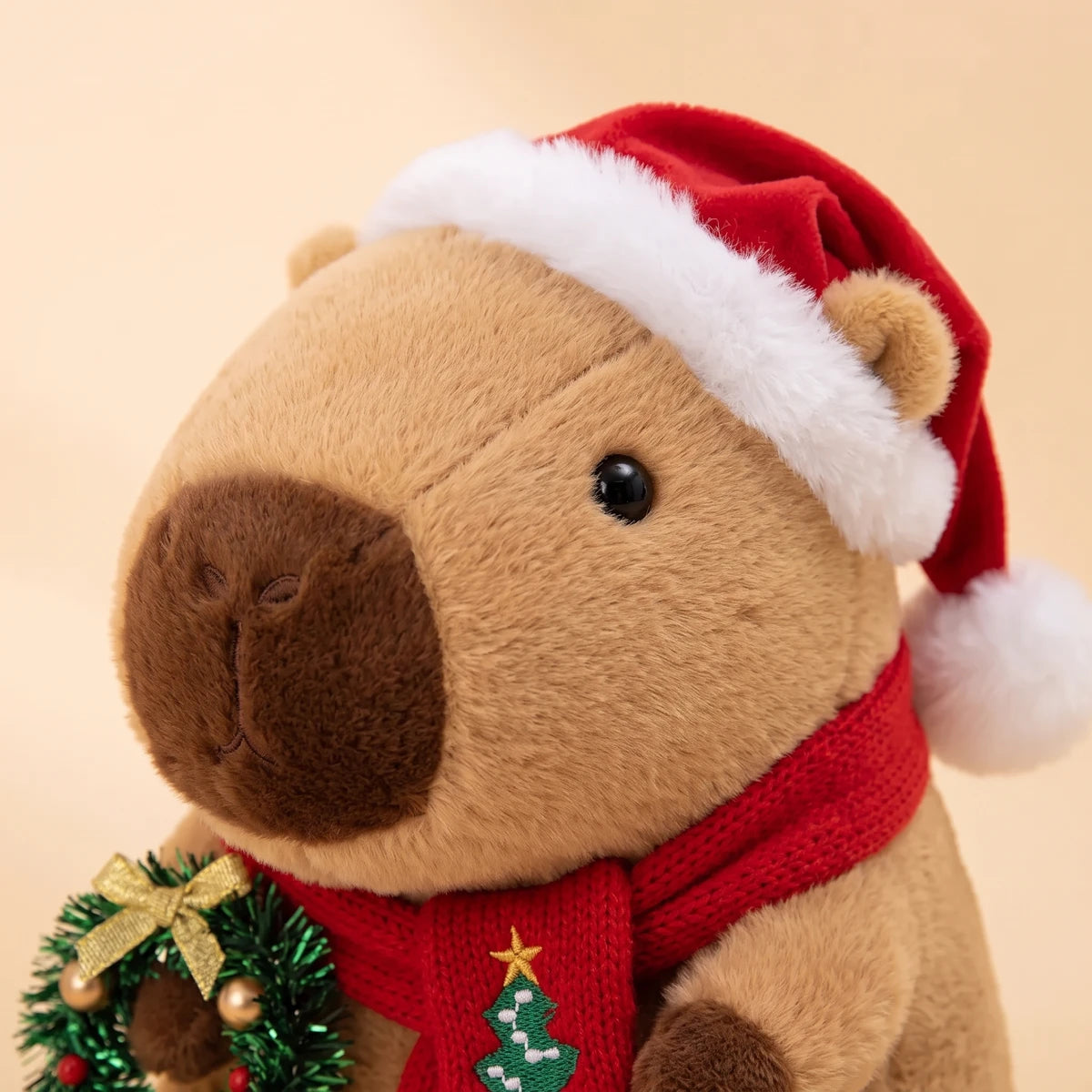 Close-up of the face of the Christmas capybara plush with a Santa hat holding a green wreath