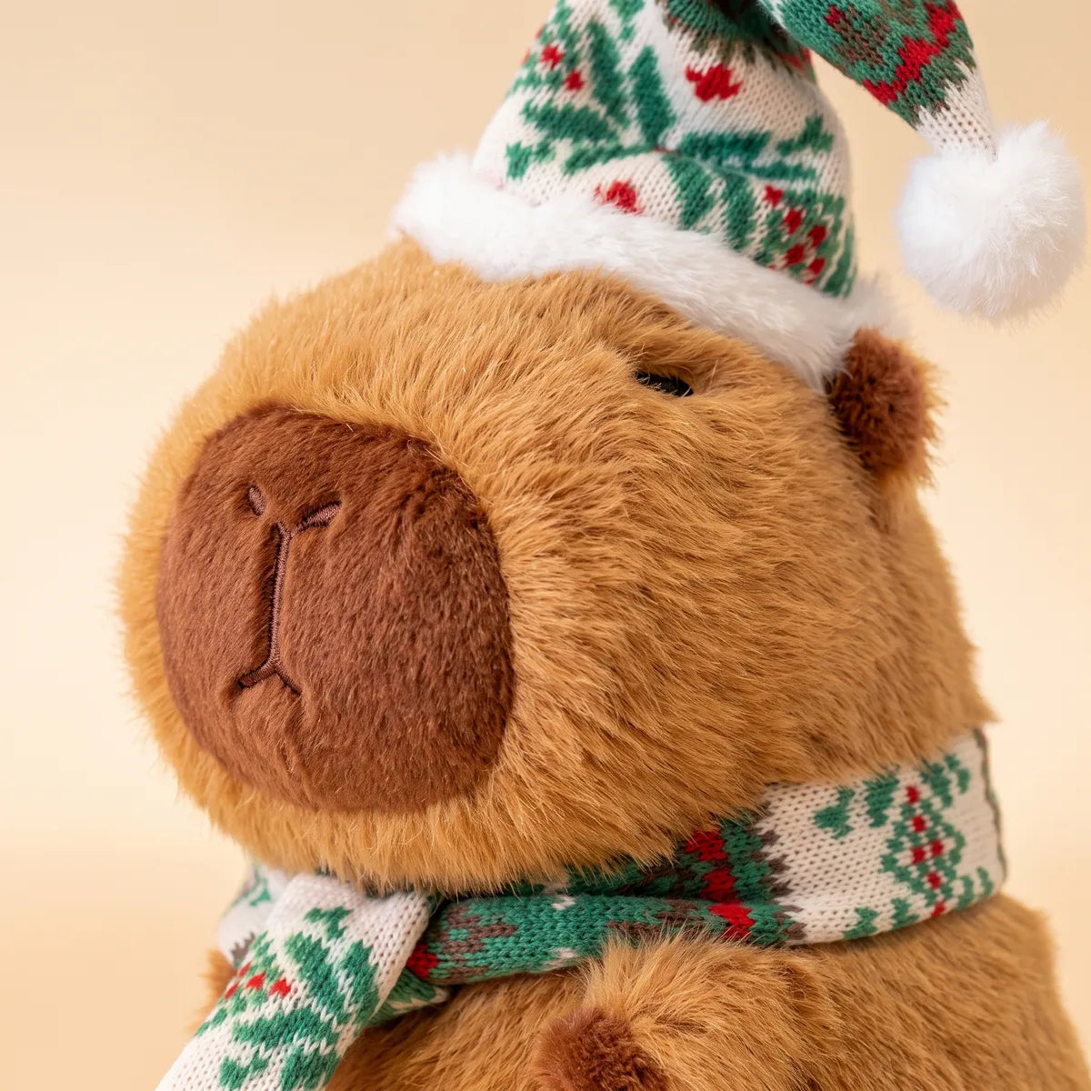 Close-up of the face of the Christmas capybara plush with a green and white berry pattern knit hat