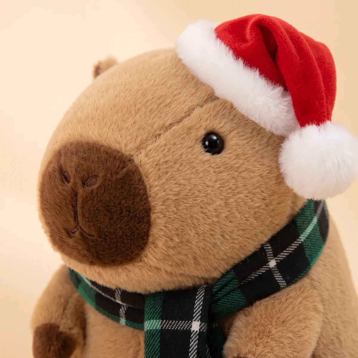Close-up of the face of the Christmas capybara plush with a Santa hat and a green plaid scarf