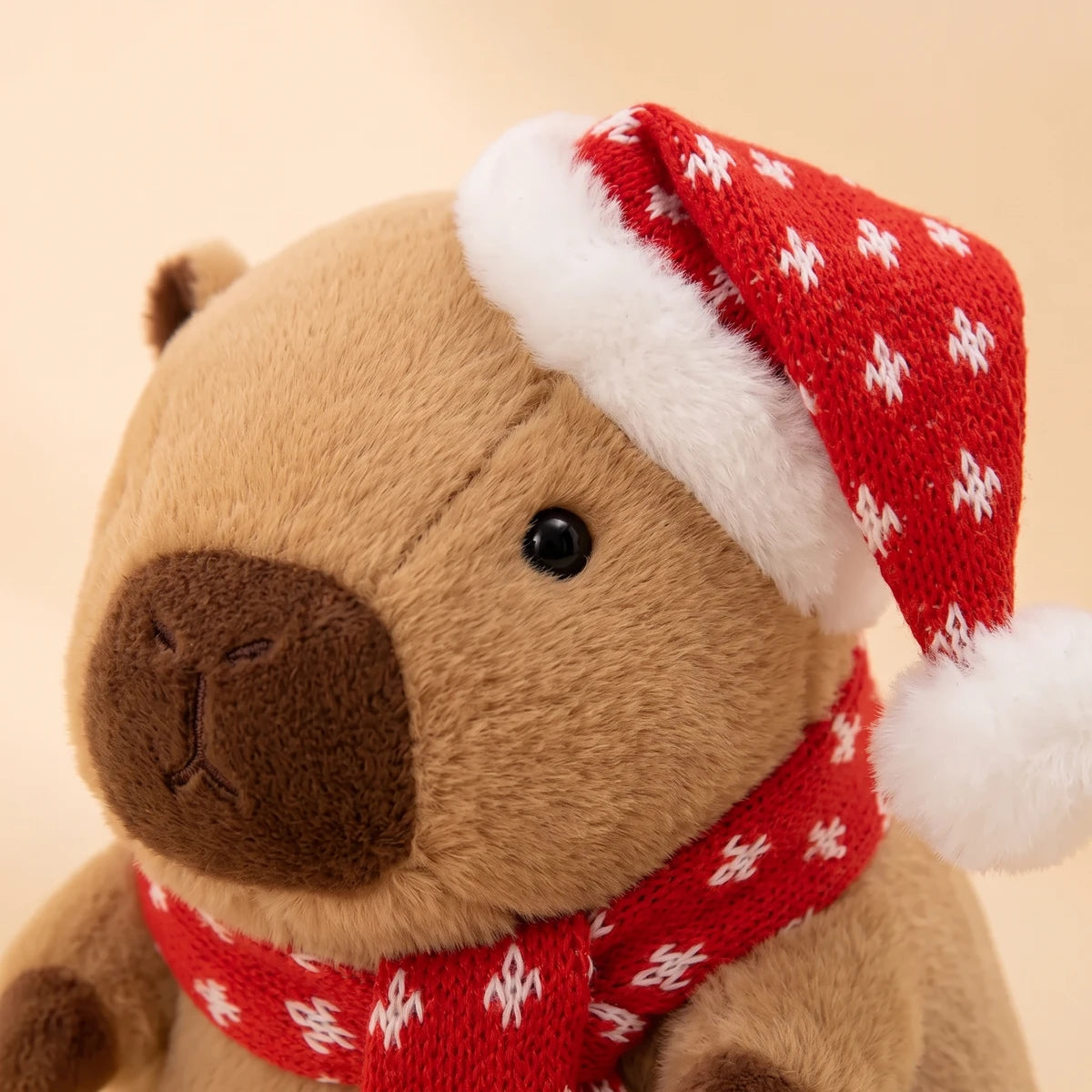 Close-up of the face of the Christmas capybara plush with a red knit hat and scarf dotted with snowflakes