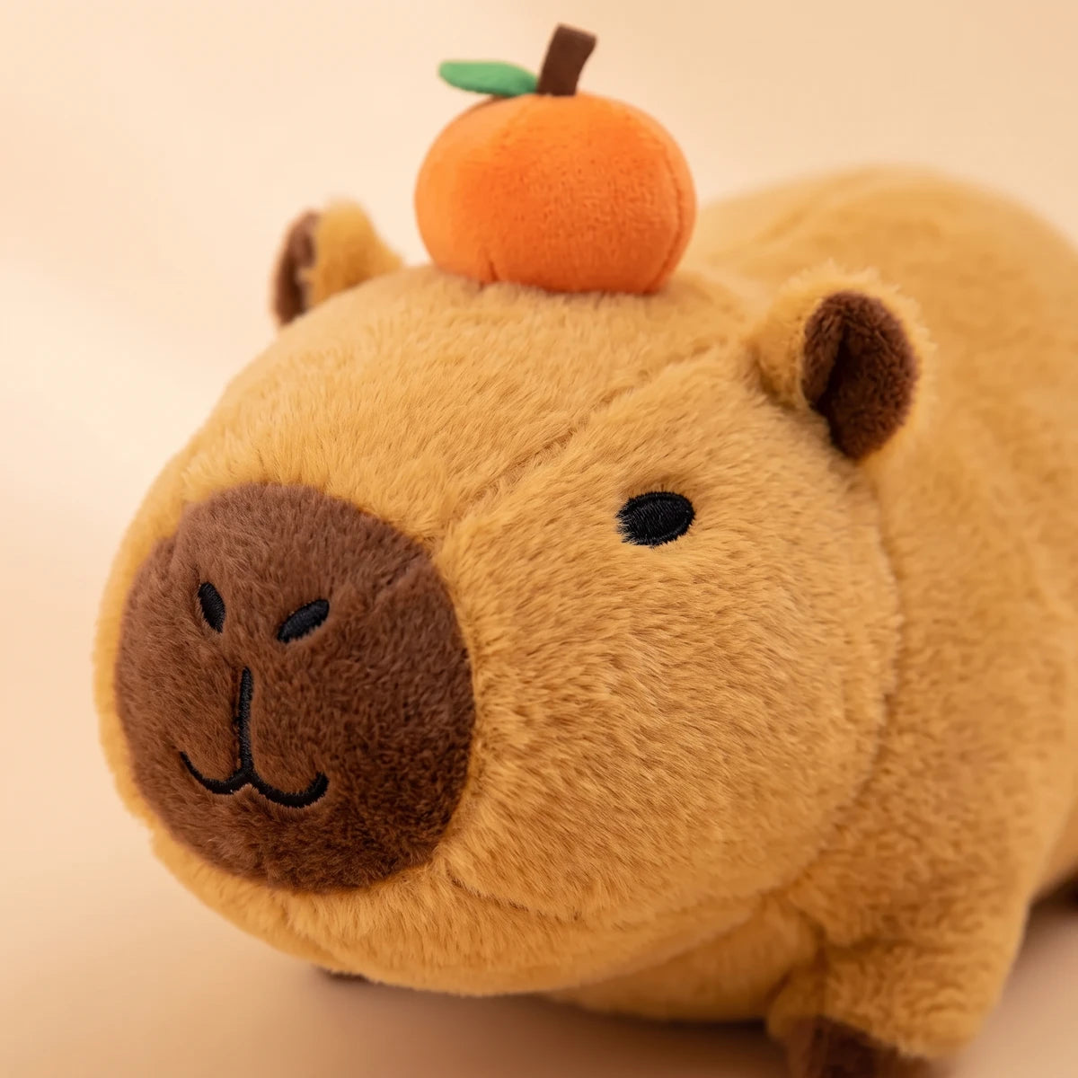 Close-up of the lying capybara plush face with the orange on its head