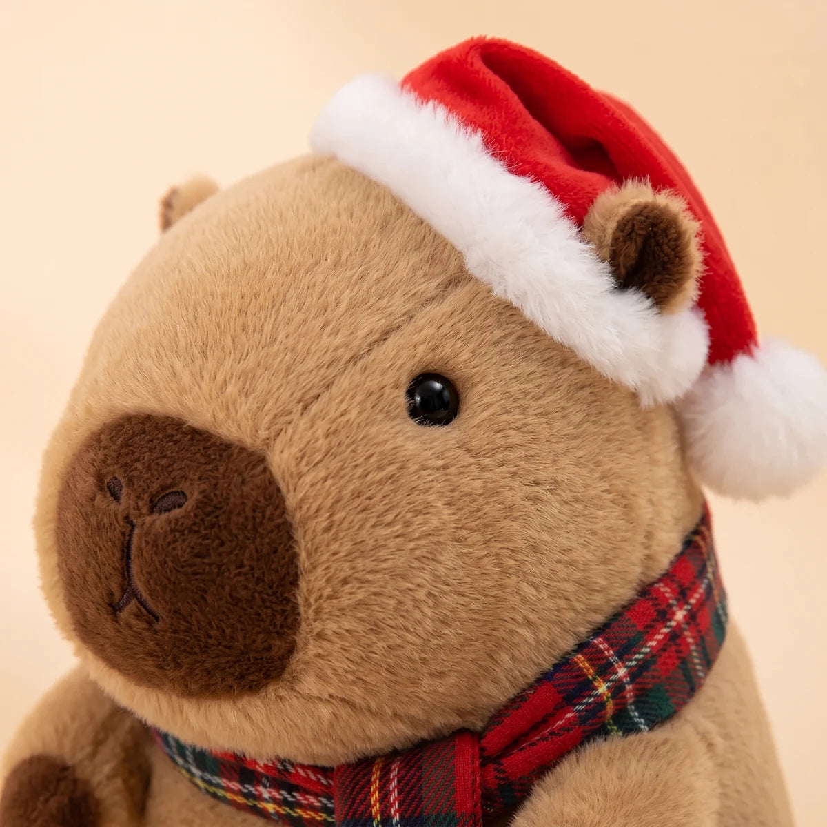 Close-up of the face of the Christmas capybara plush with a Santa hat and a red tartan scarf