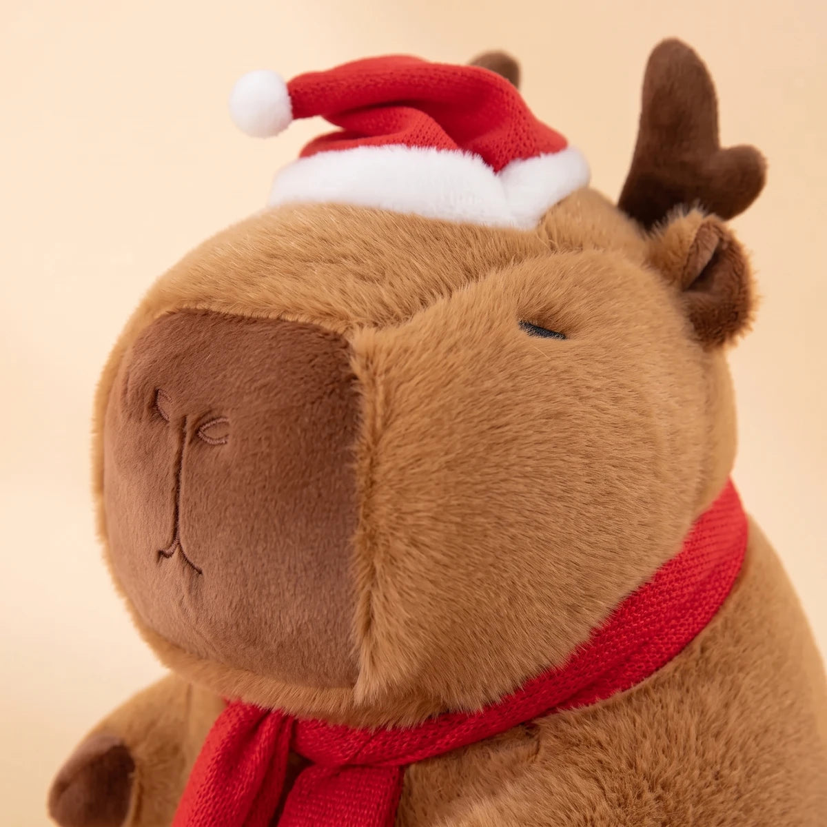 Close-up of the reindeer capybara plush face with its antlers and small Santa hat
