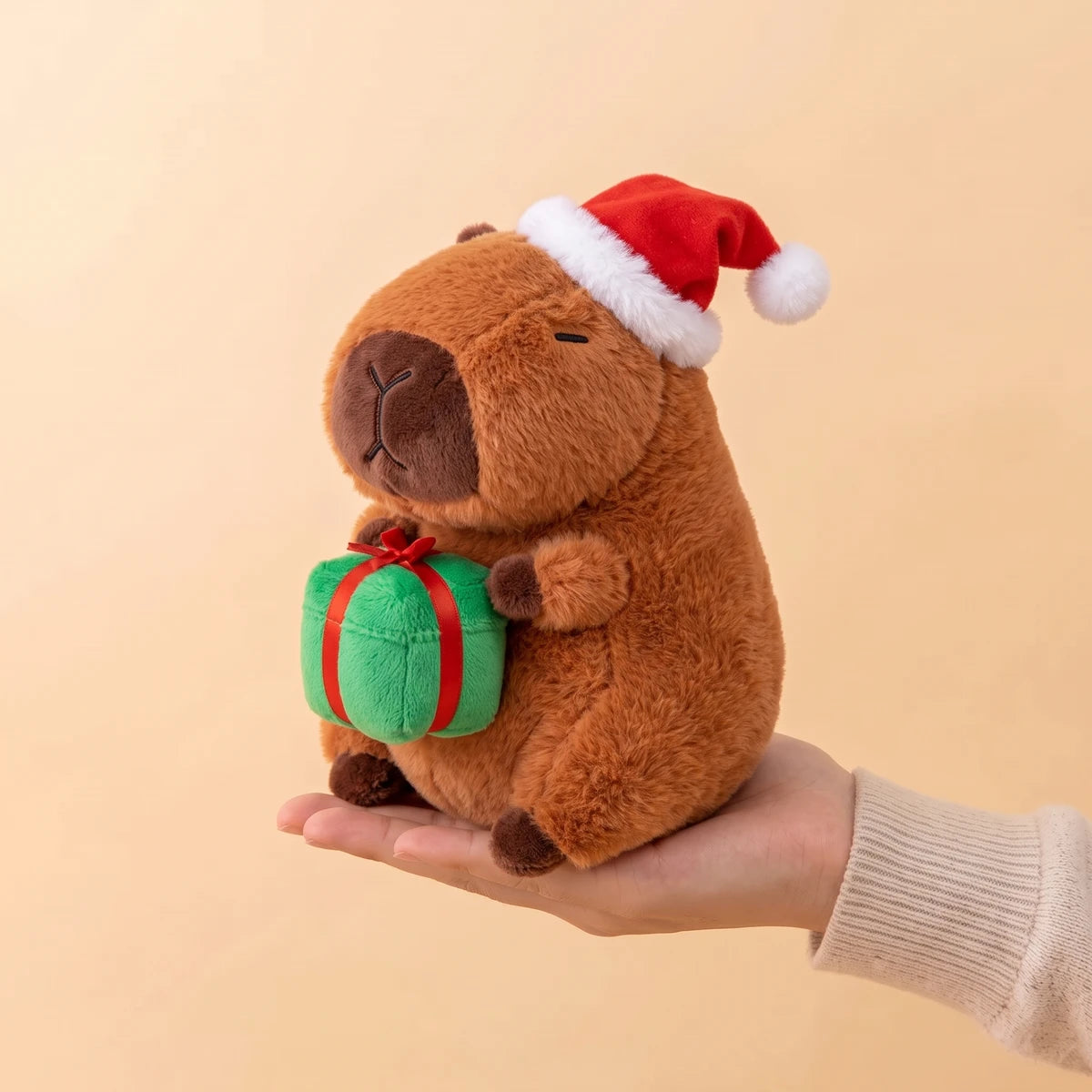 Santa hat capybara plush sitting on an open hand to show its 8 in size
