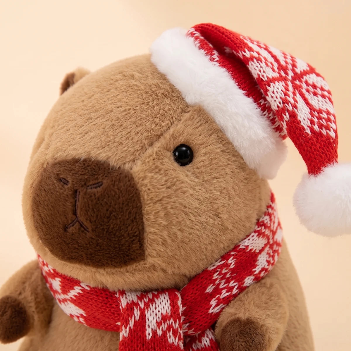 Close-up of the face of the Christmas capybara plush with a red snowflake knit hat and scarf