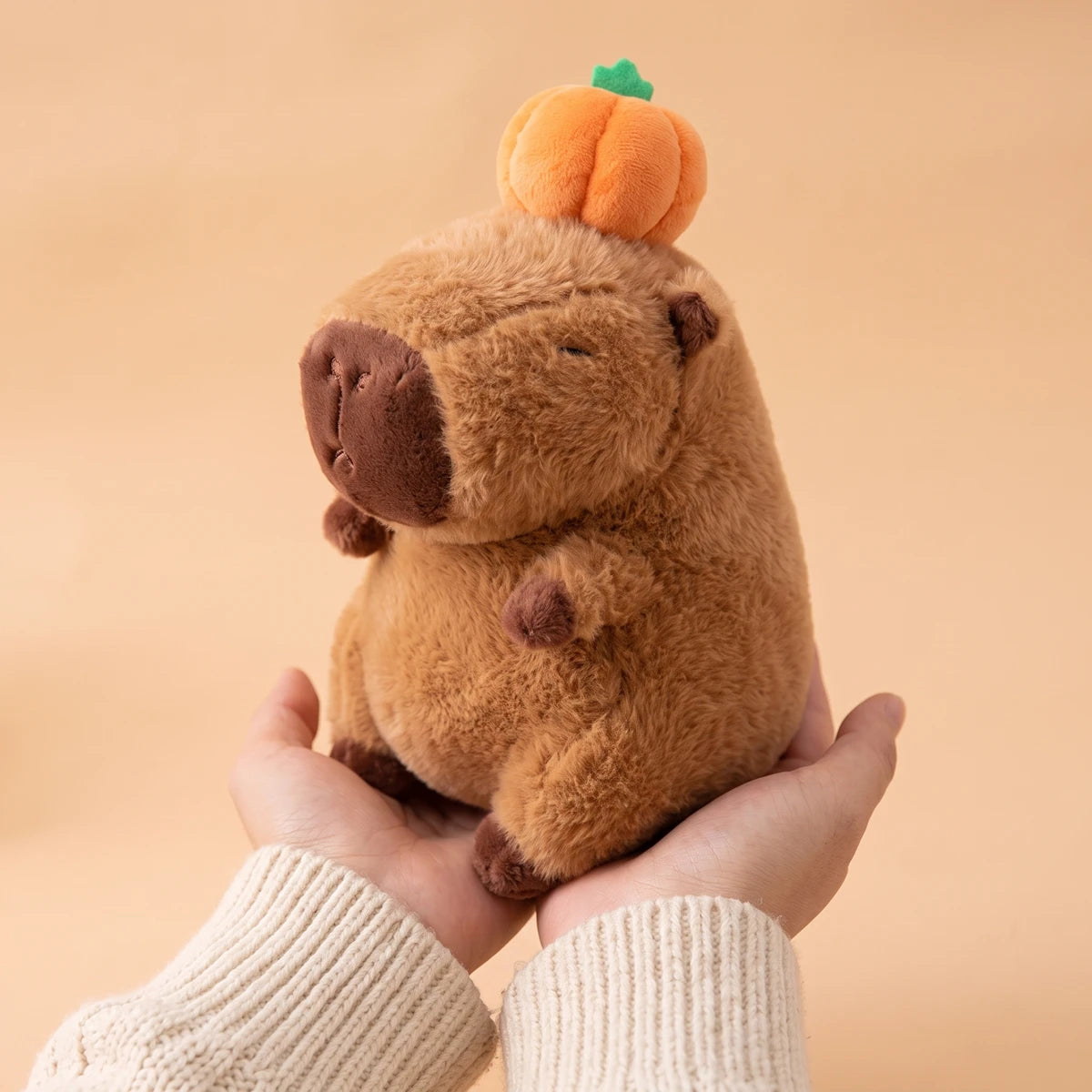 Capybara with pumpkin on head plush held in two hands to show its 10 in size