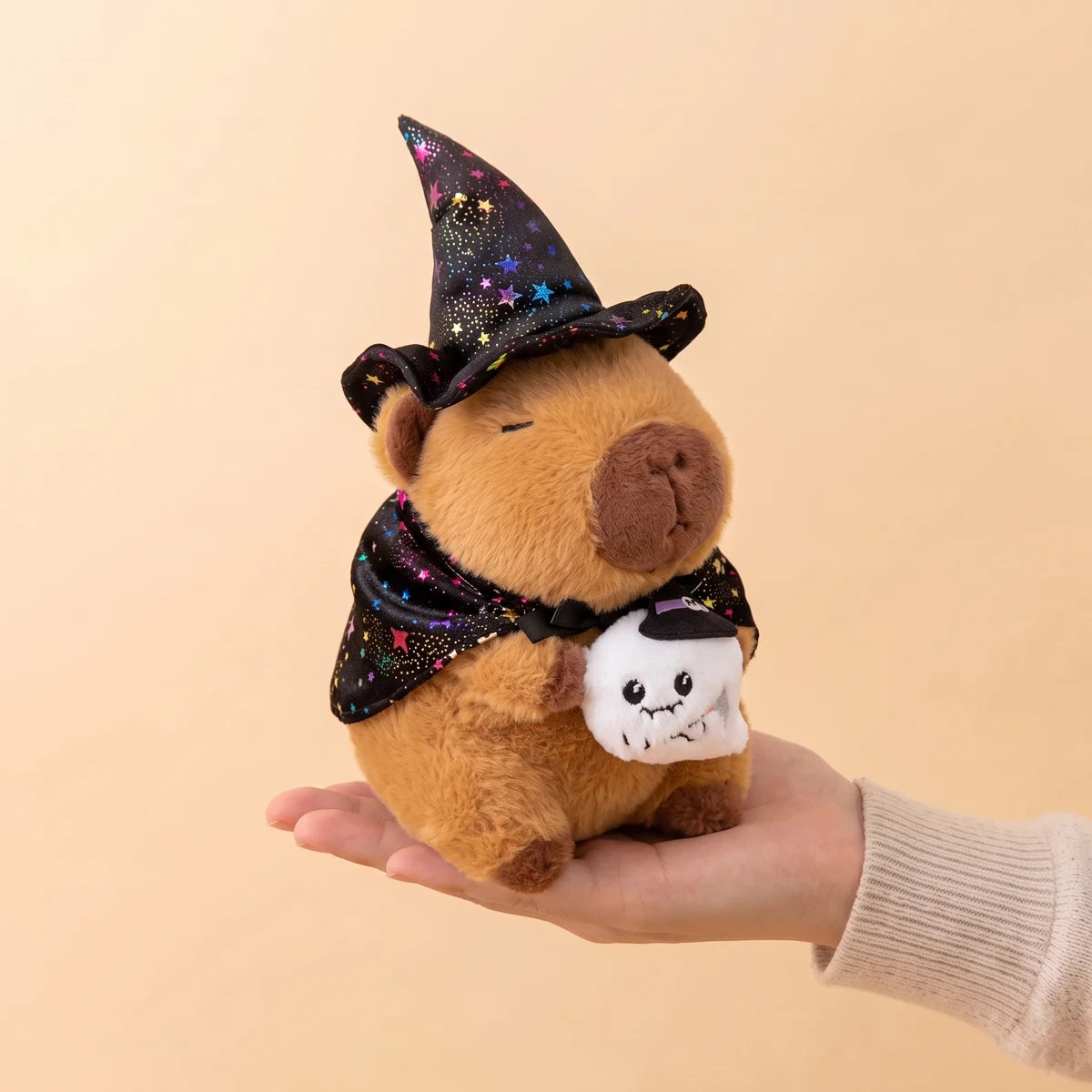 Ghost witch capybara plush holding a small ghost, sitting on an open hand