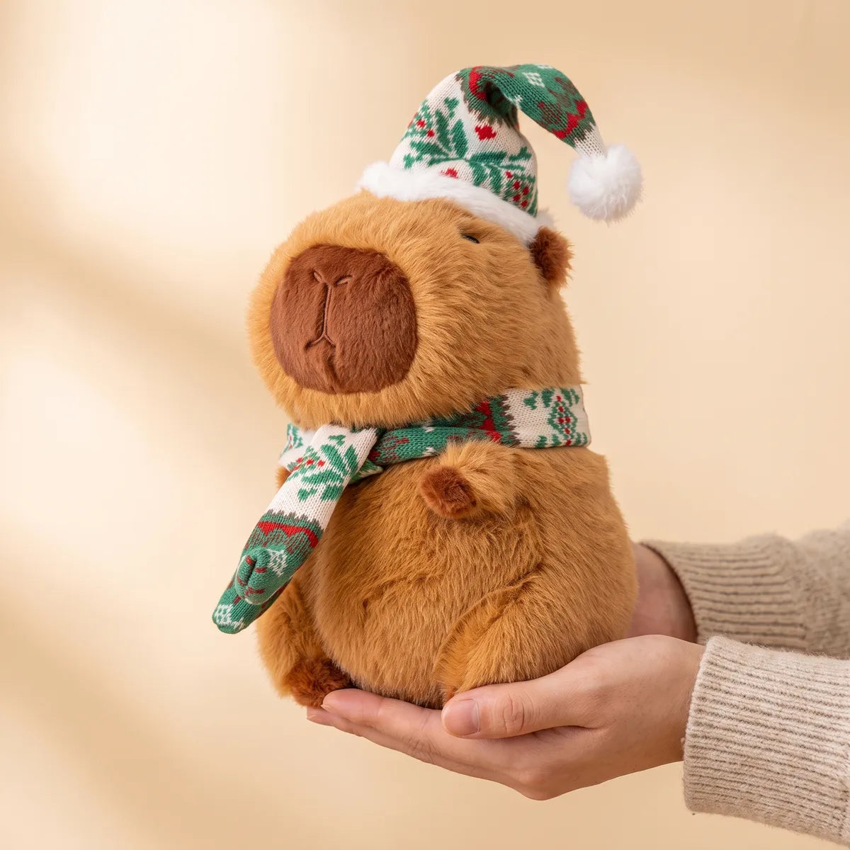 10 in Christmas capybara plush with a green and white knit hat and scarf held in two hands