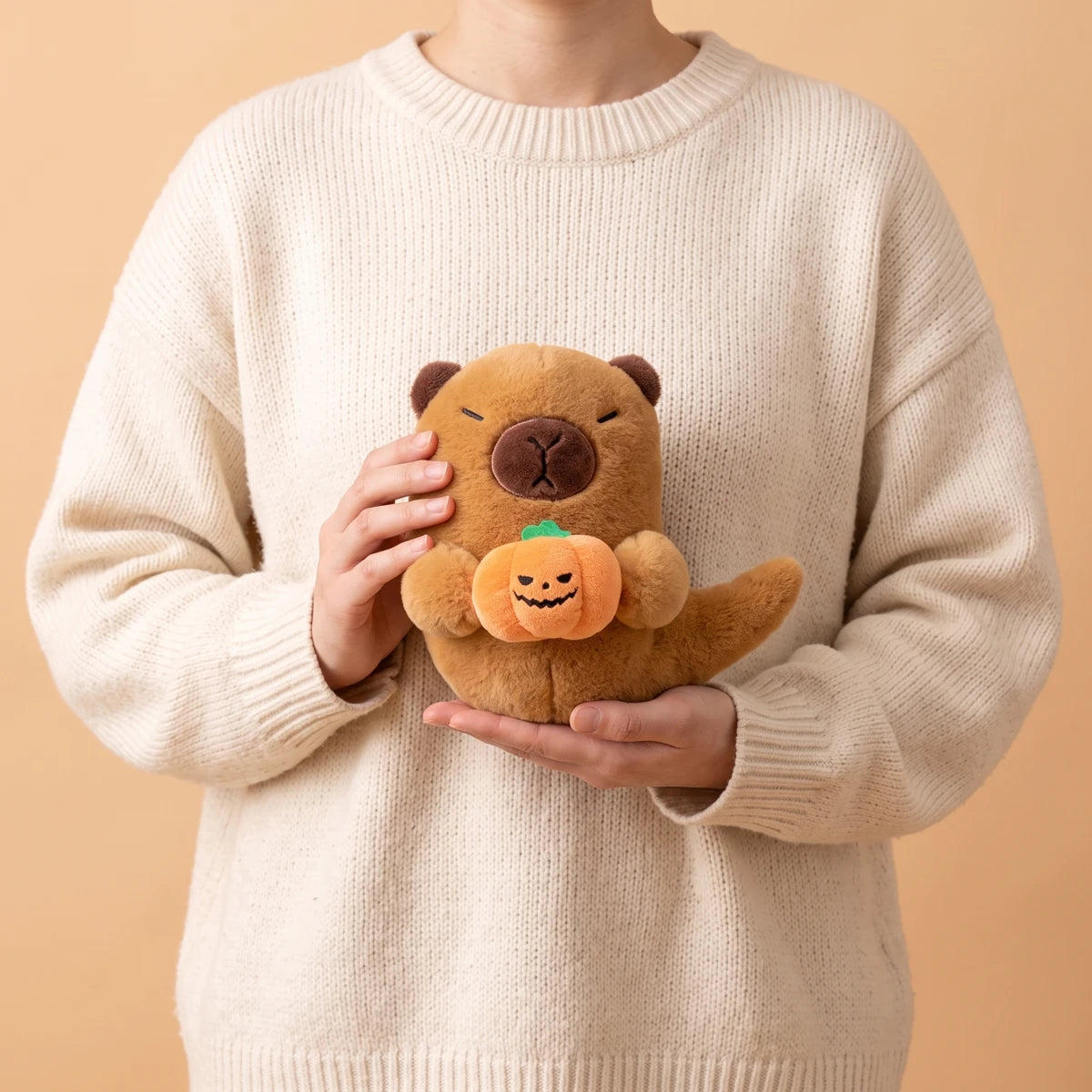 Person in a cream sweater holding the 7 in Halloween ghost capybara plush in both hands