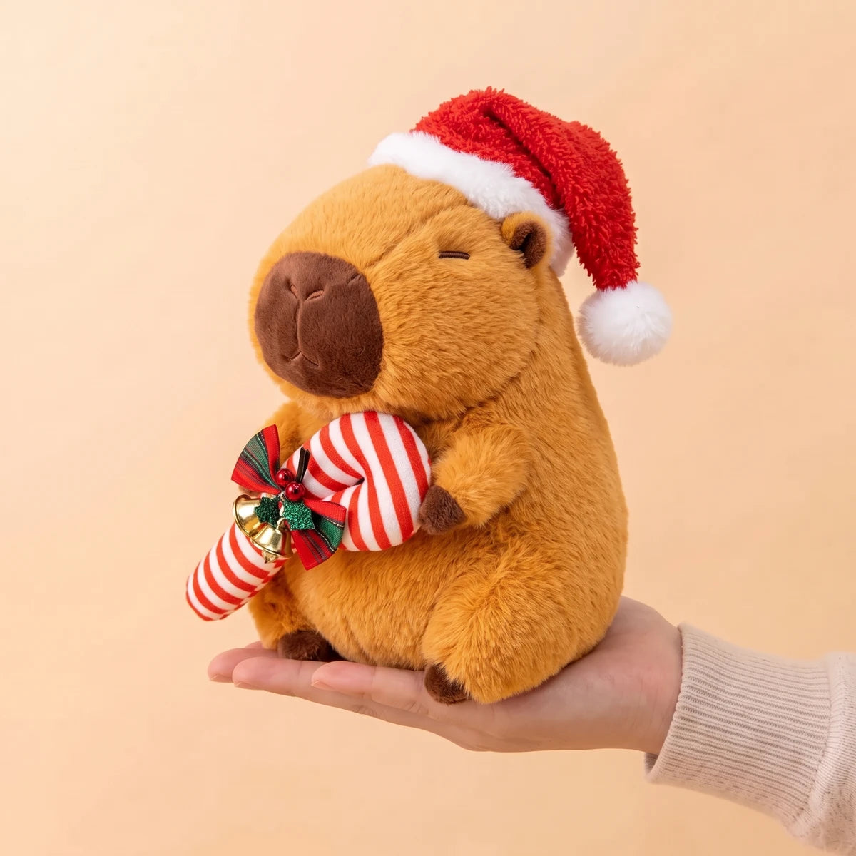 10 in Christmas capybara plush with a candy cane sitting on an open hand