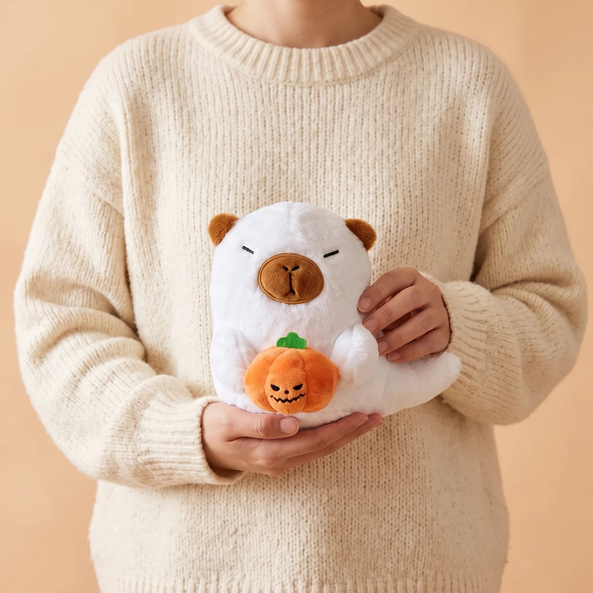 Person in a cream sweater holding the white ghost capybara plush