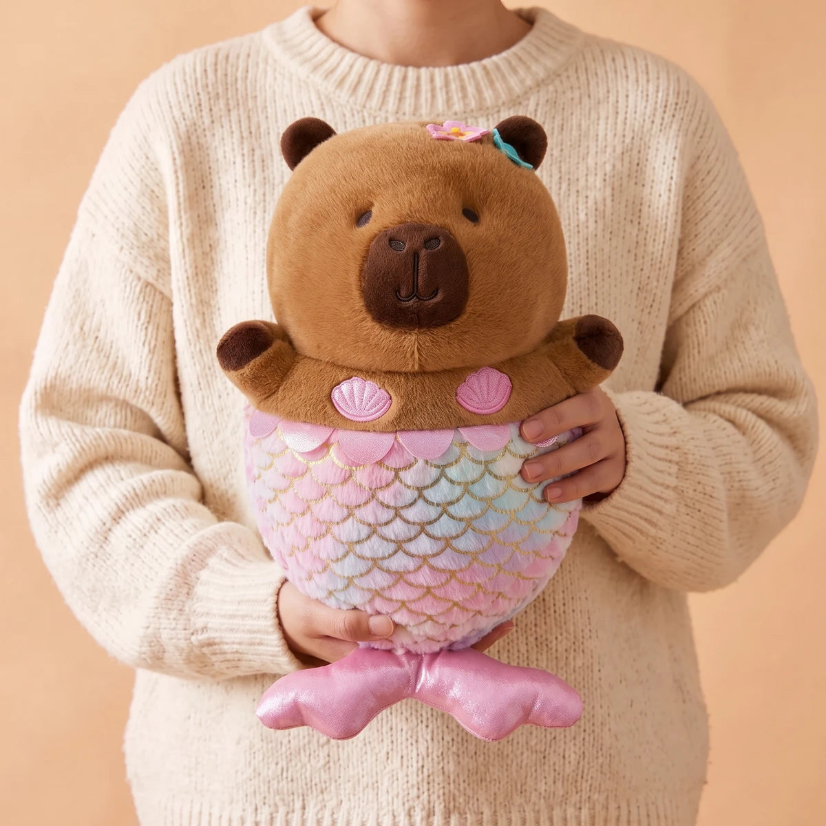 Person in a cream sweater holding the mermaid capybara plush