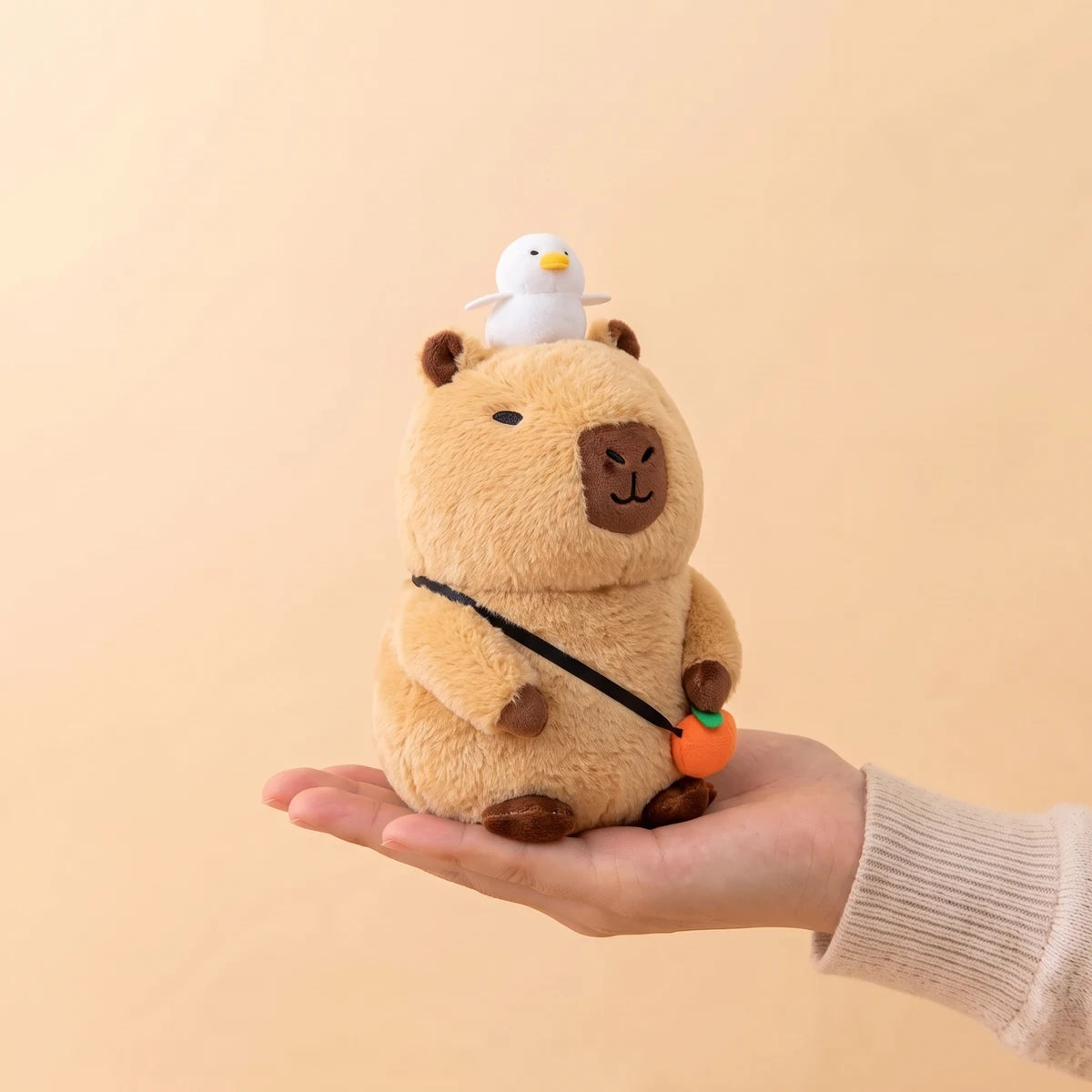 8 in capybara plush with orange bag sitting on an open hand