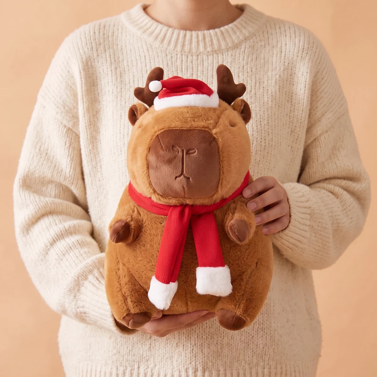 Person in a cream sweater holding the reindeer capybara plush