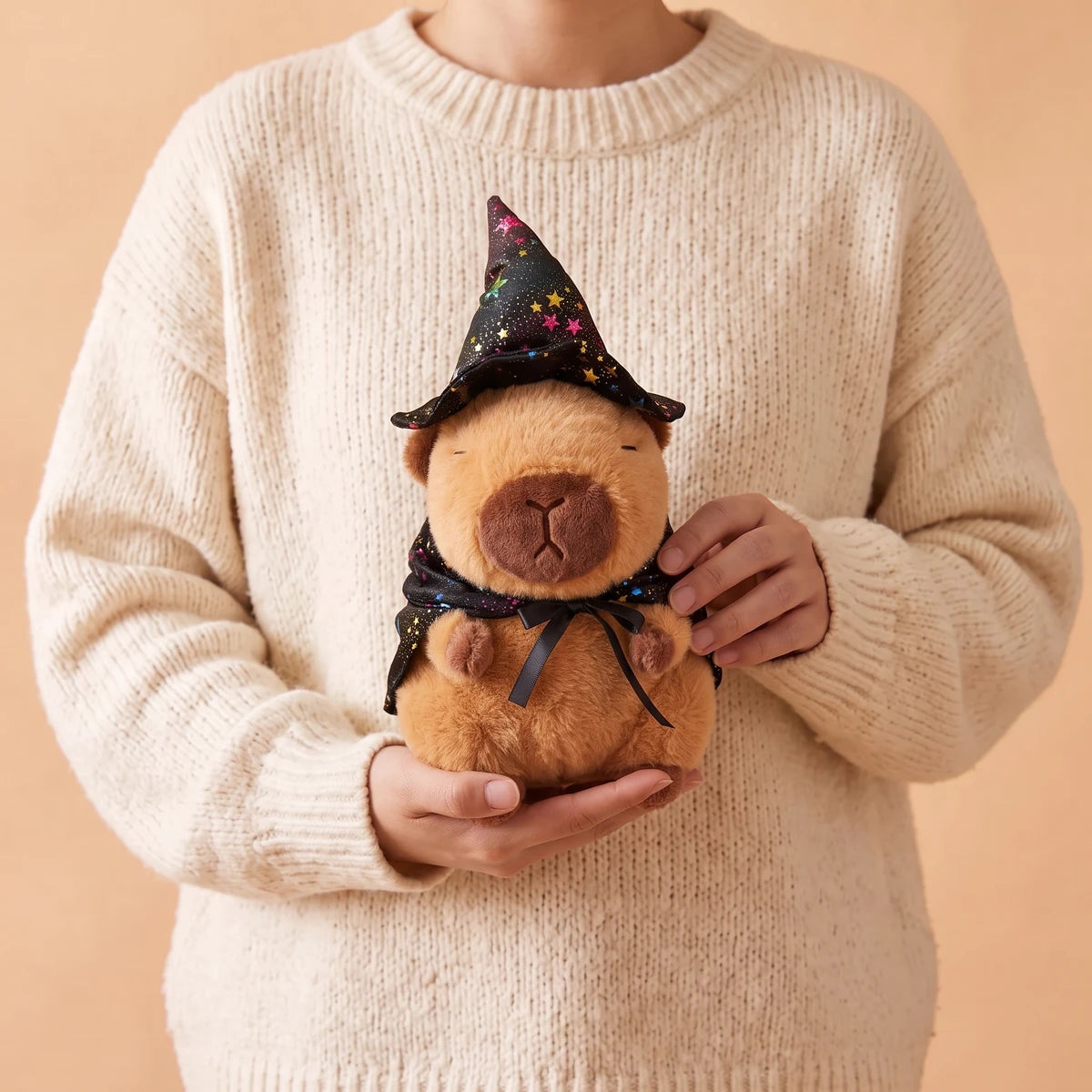 Person in a cream sweater holding the witch capybara plush with a starry black hat and cape