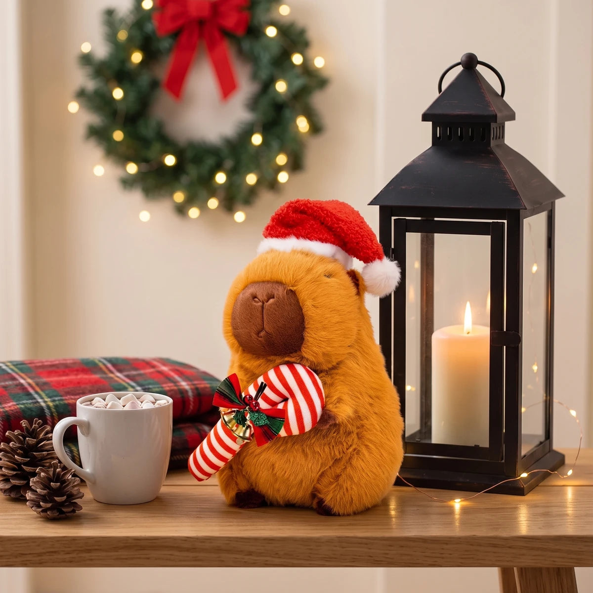 Christmas capybara plush with a candy cane on a bench next to a lantern and a mug of hot chocolate