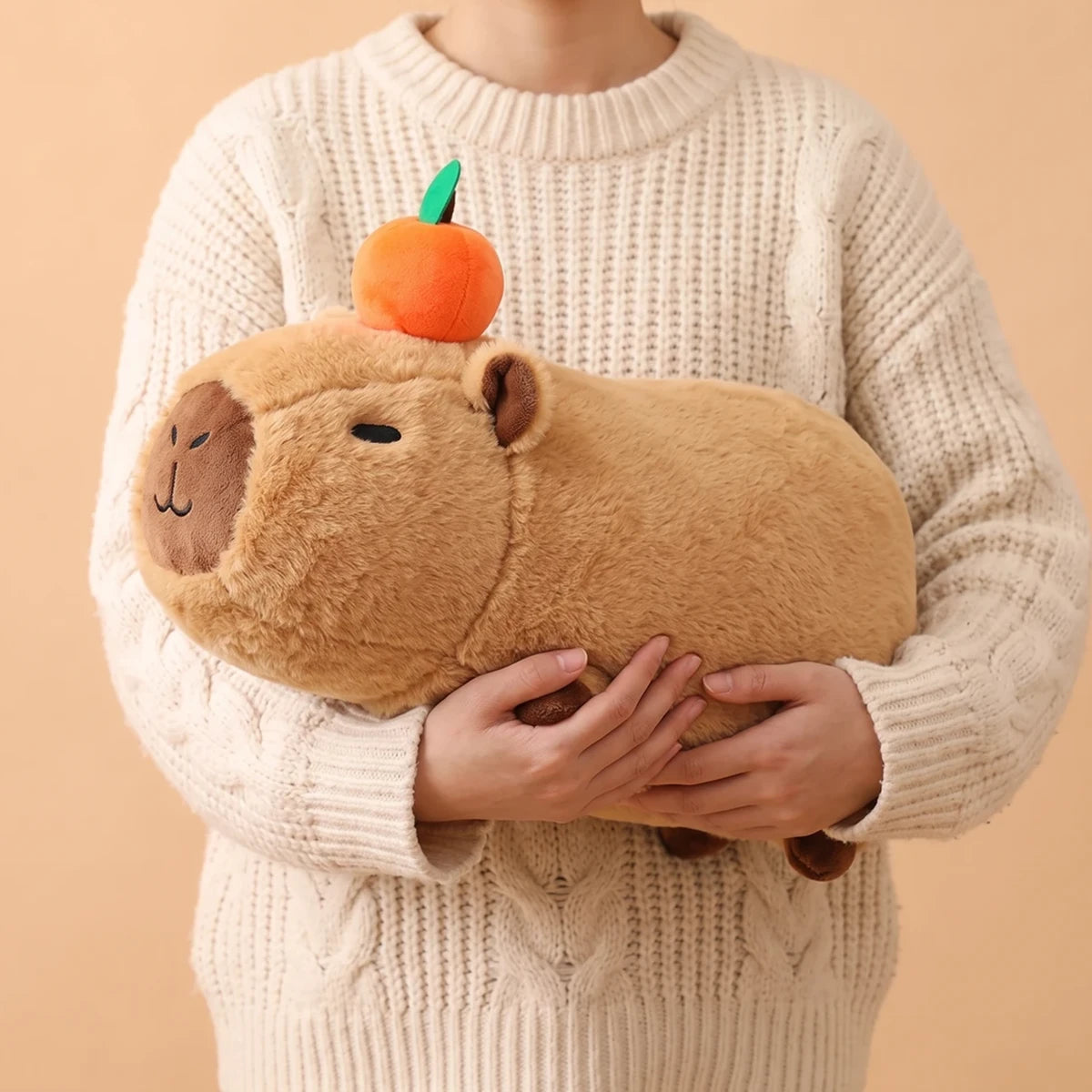 Person in a cream sweater holding the 16 in lying capybara plush in both arms