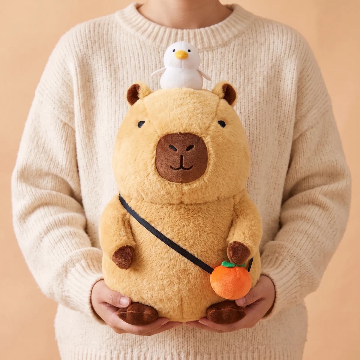 Person in a cream sweater holding the 16 in capybara plush with orange bag
