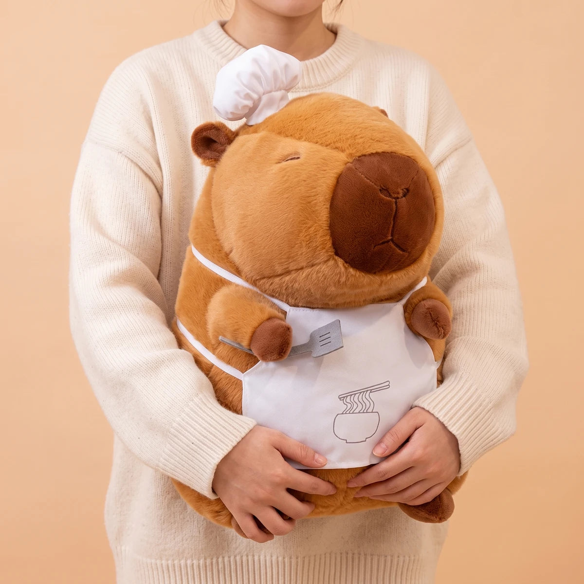 Person in a cream sweater holding the 20 in ramen chef capybara plush