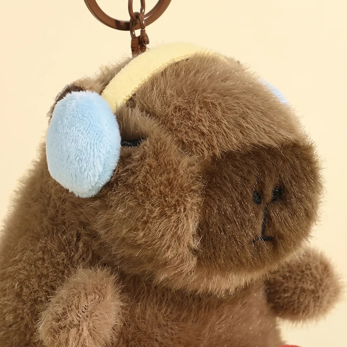 Close-up of the accordion capybara keychain wearing pale blue ear cups on a cream headband