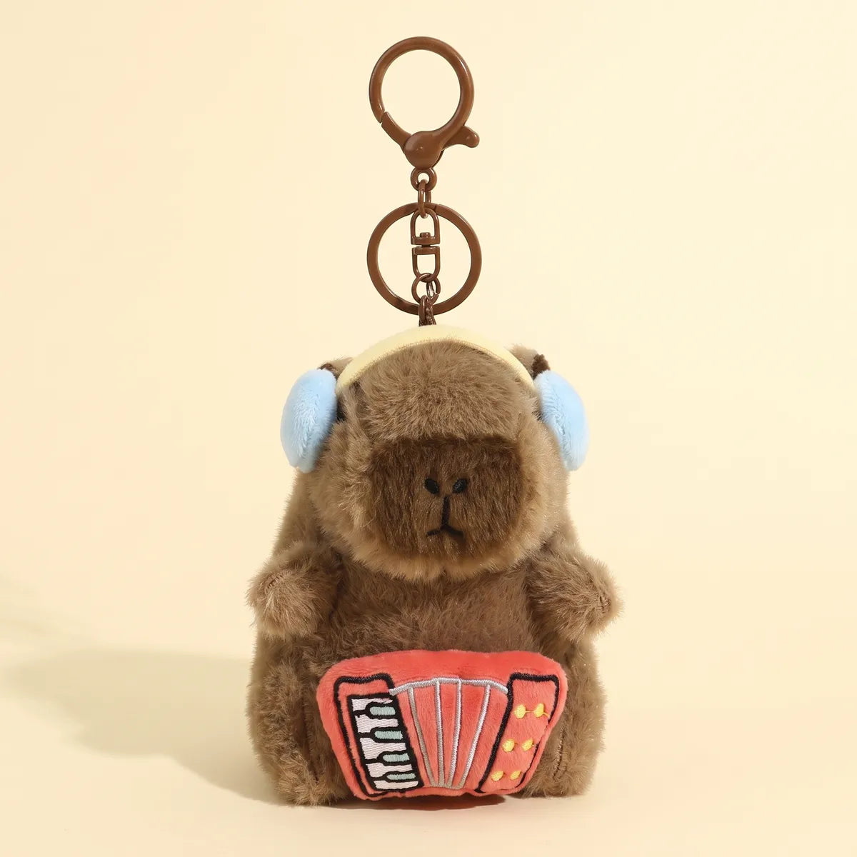 Accordion capybara keychain hanging from its bronze clasp with the red accordion facing forward