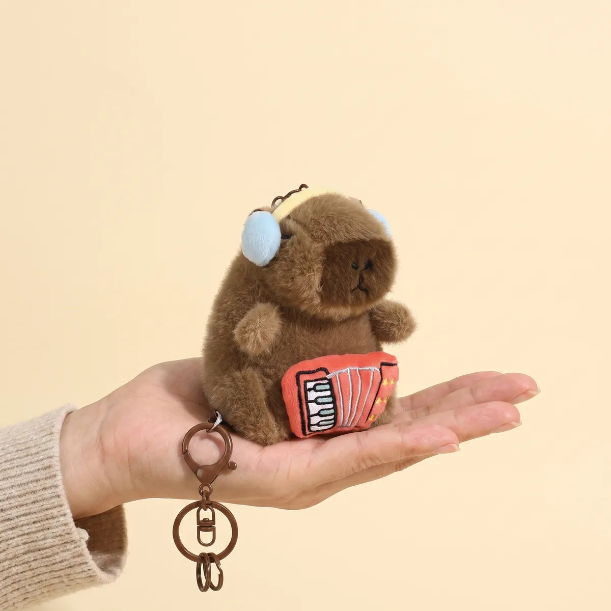 Accordion capybara keychain held in an open hand to show its 4 in charm size