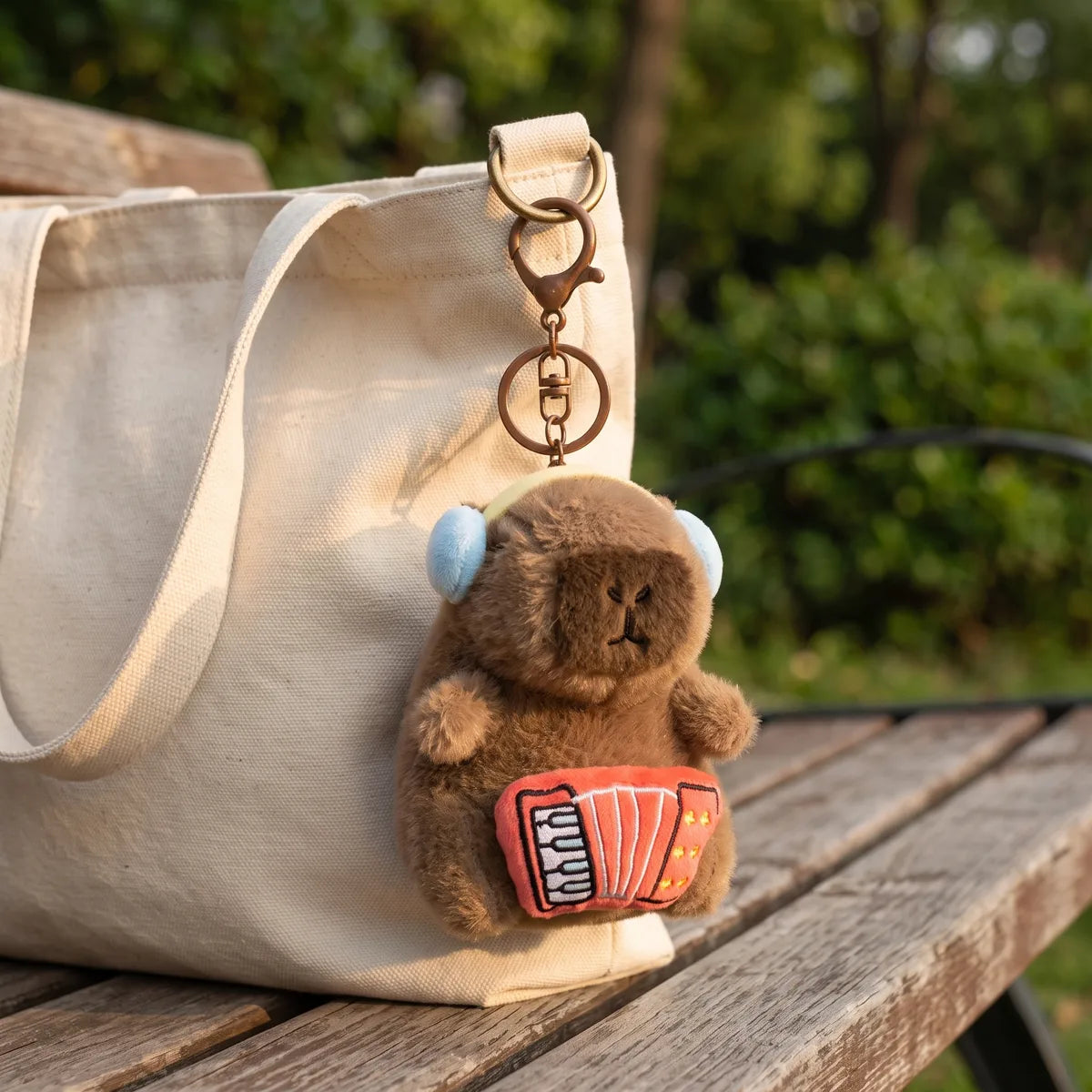 Accordion capybara keychain clipped to a cream tote bag resting on a wooden bench outdoors