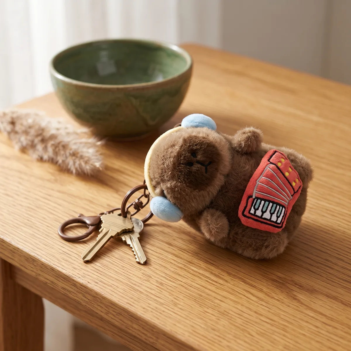Accordion capybara keychain lying on a wooden table next to house keys and a green ceramic bowl