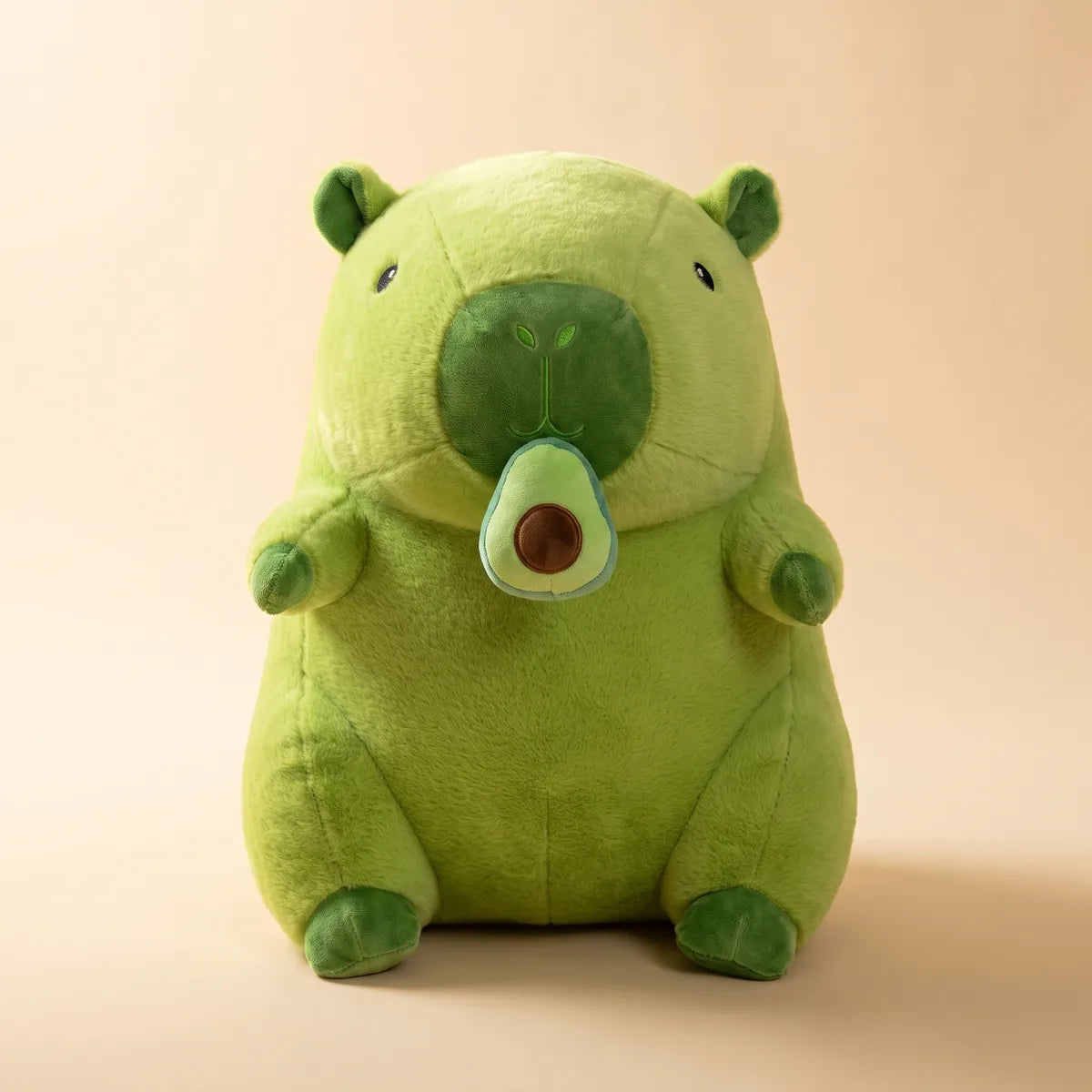 Front view of the 12 in avocado capybara plush holding its plush avocado half against a beige backdrop