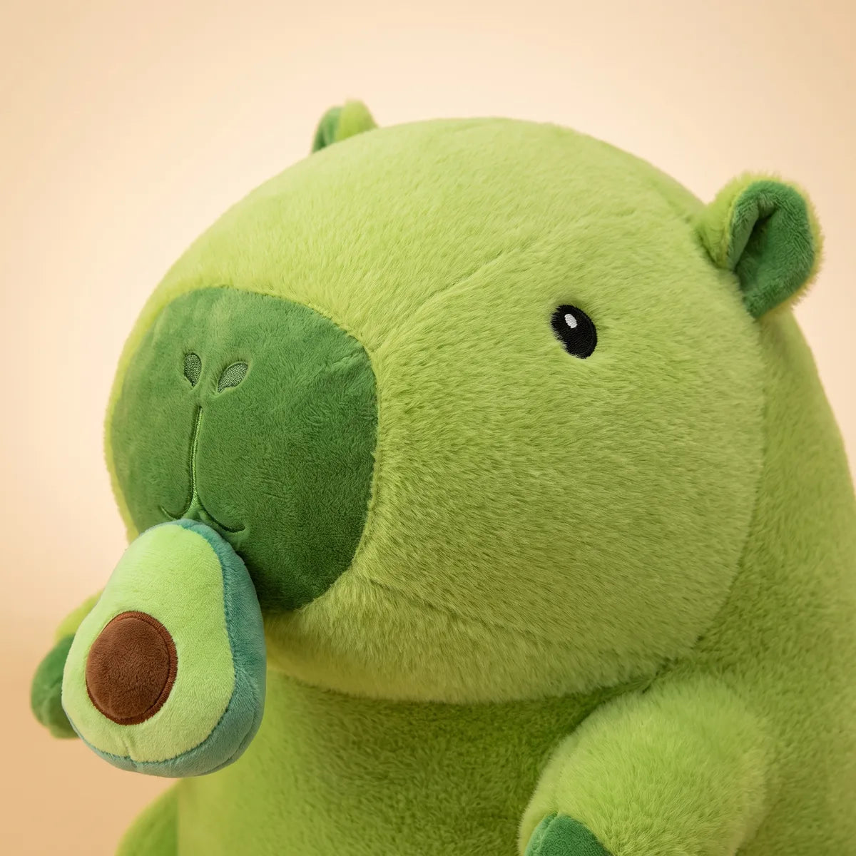 Close-up of the avocado capybara plush head showing its glossy black eyes and dark green muzzle