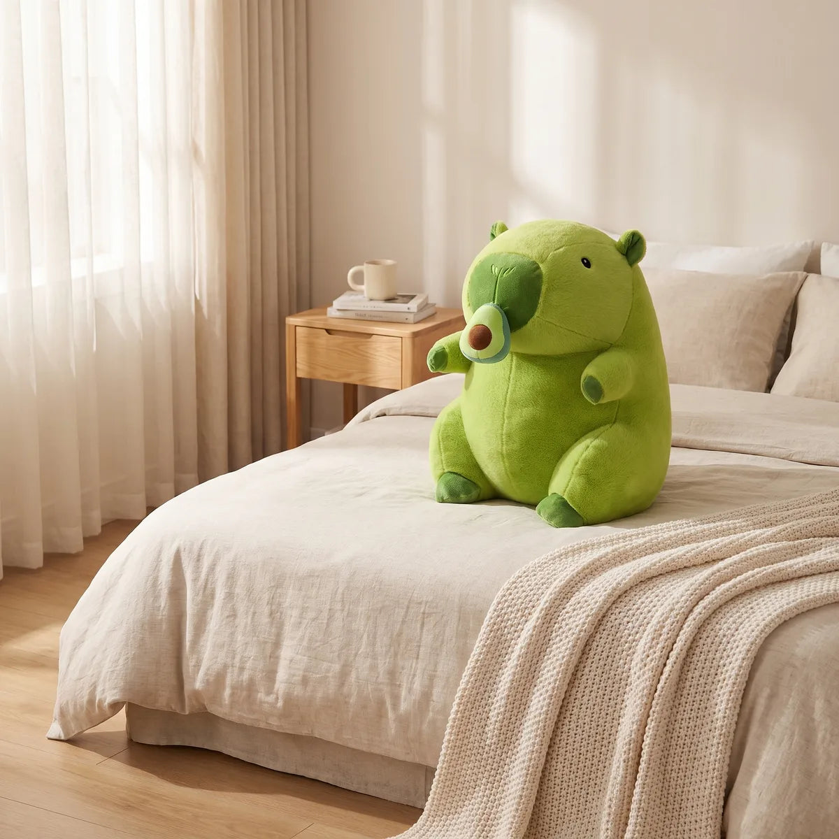 Green avocado capybara plush sitting on a cream linen bed beside a pale knit throw