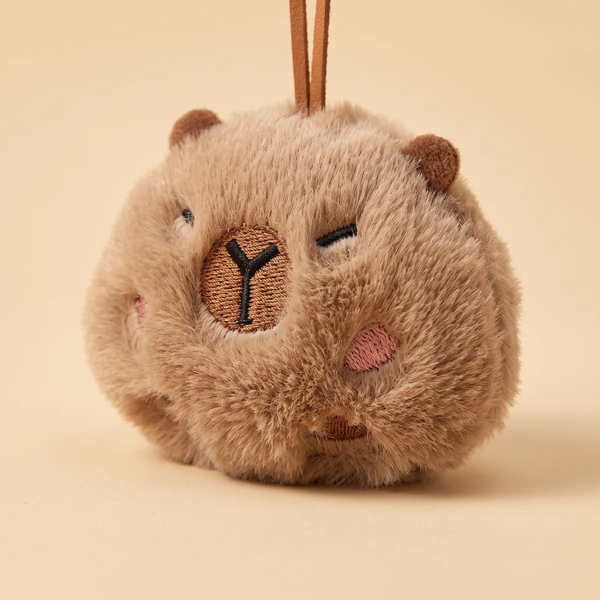Close up of the ball capybara keychain embroidered face with closed eyes and pink cheeks