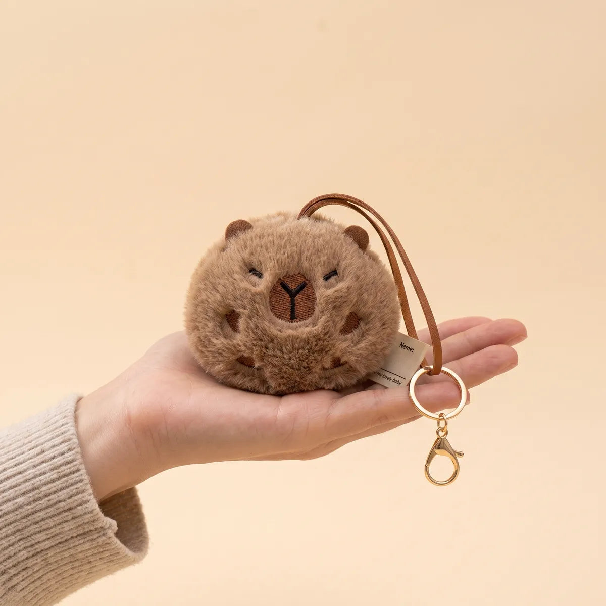Ball capybara keychain in an open palm with its gold clasp and split ring