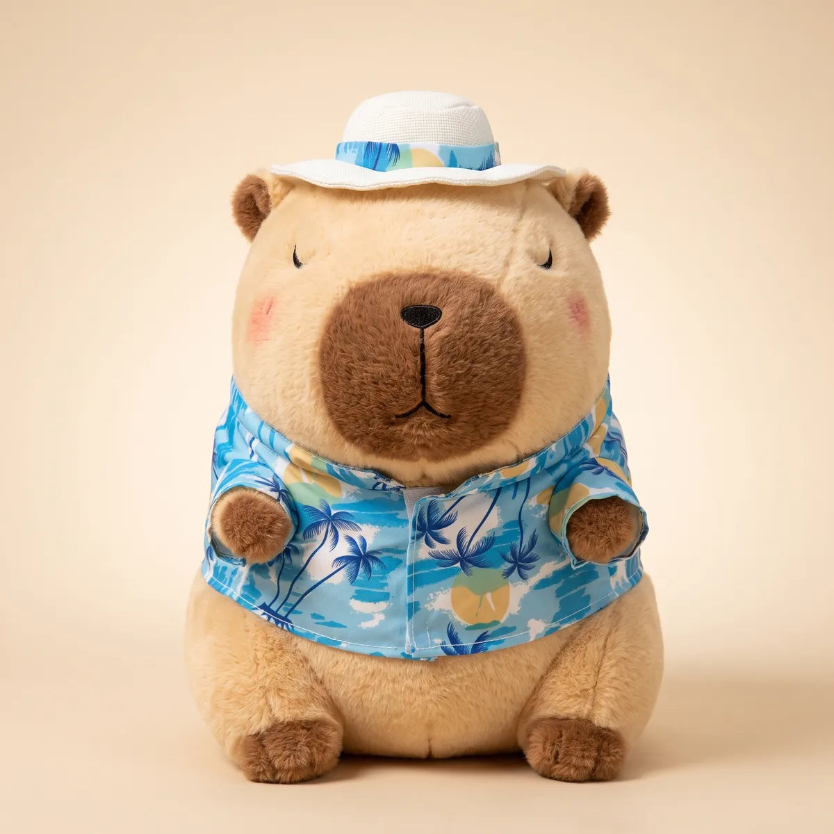 Front view of the brown capybara stuffed animal seated in its blue palm print beach shirt and white sun hat