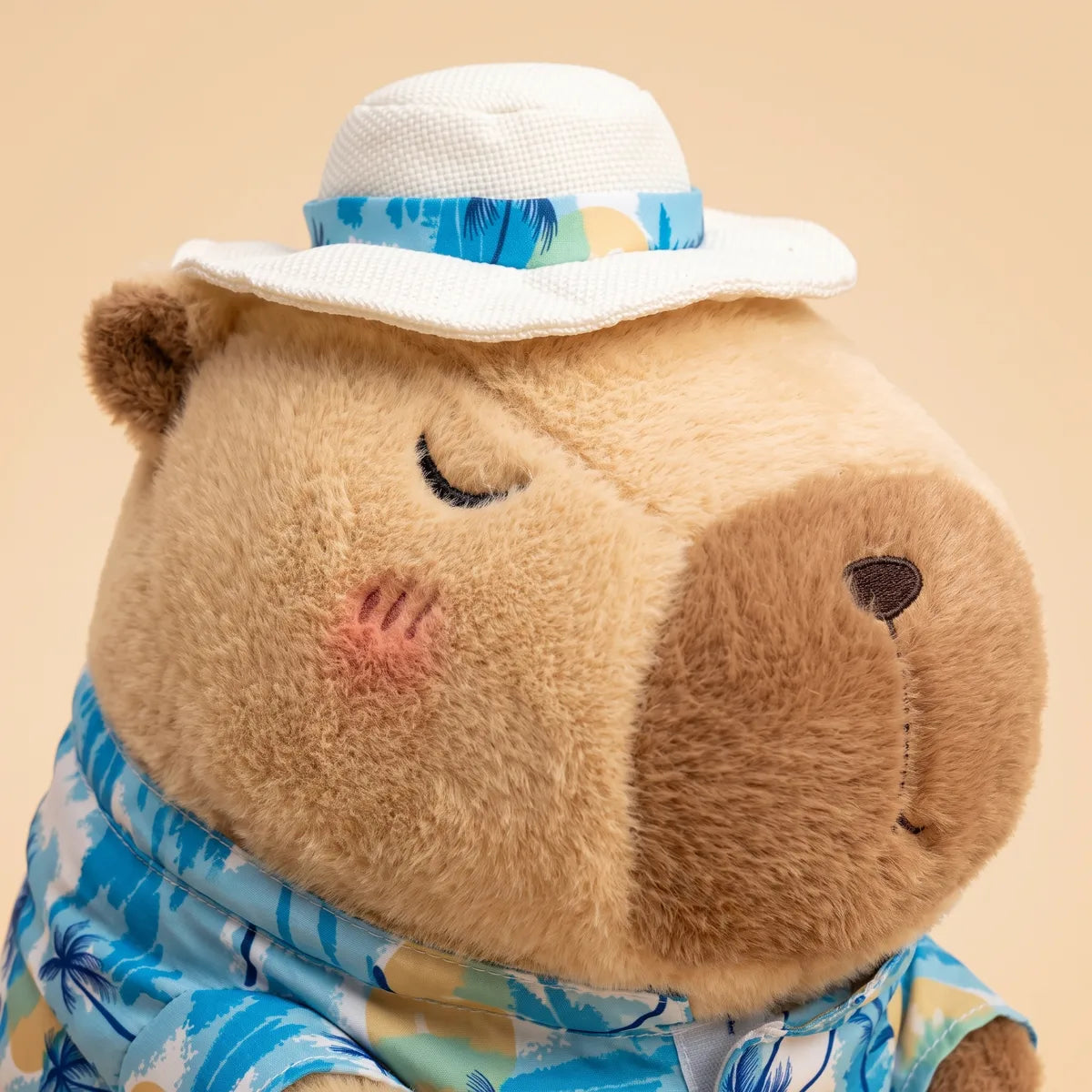 Close-up of the brown capybara stuffed animal head with its dark chocolate muzzle, pink blush cheek and stitched closed eye