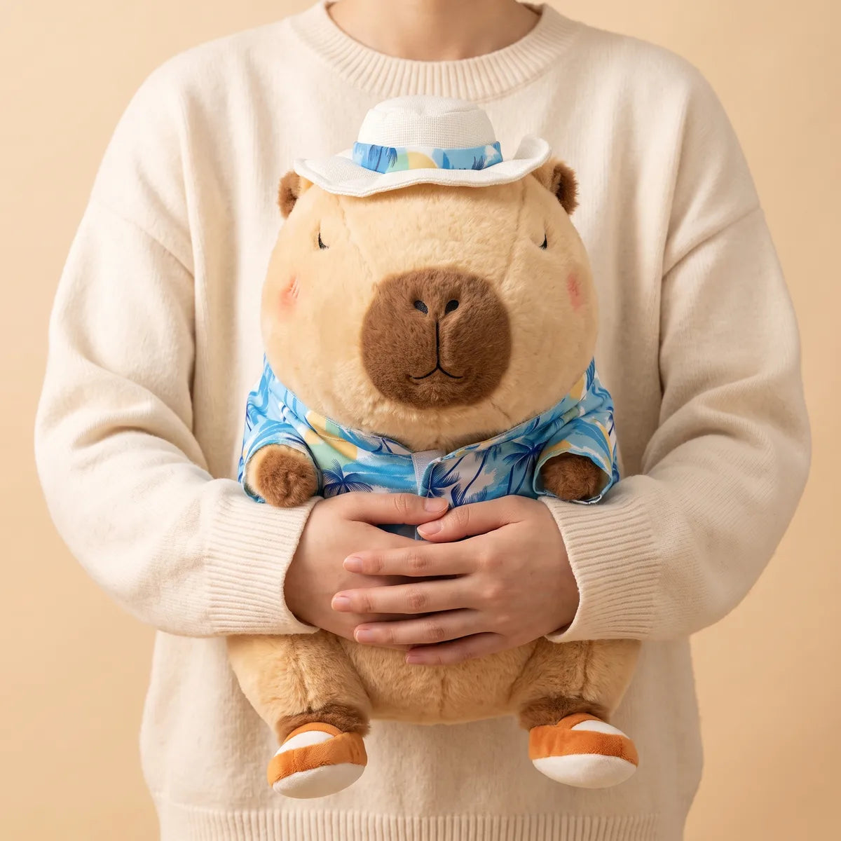 Person in a cream sweater cradling the brown capybara stuffed animal, its orange and white sandal feet visible