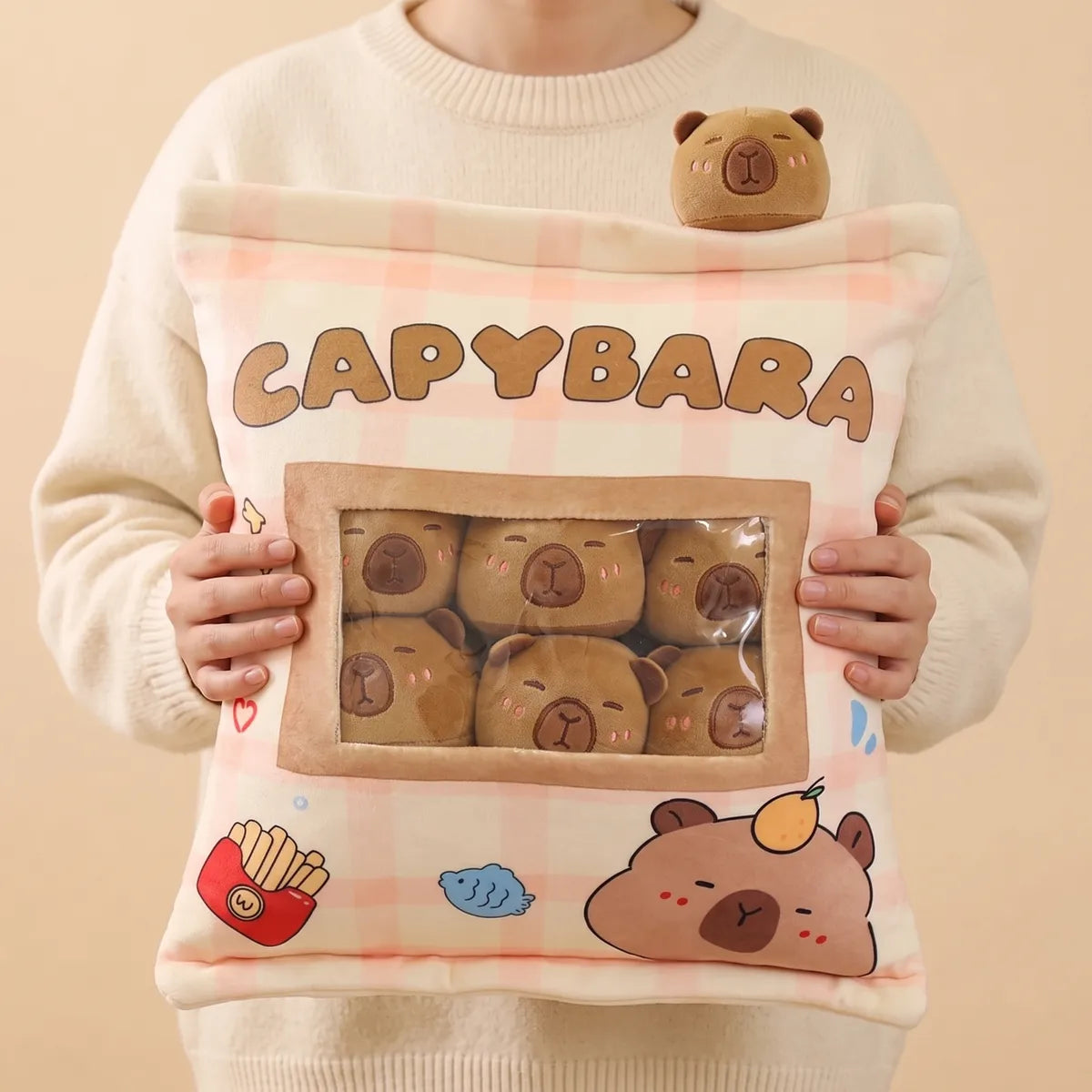 Person holding the brown mini capybara plush set with both hands, one tan mini resting on their shoulder