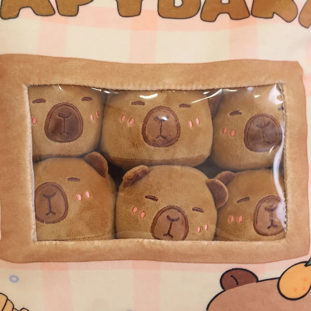 Close-up of six brown mini capybara plush stacked two rows deep behind the clear window of the bag pillow