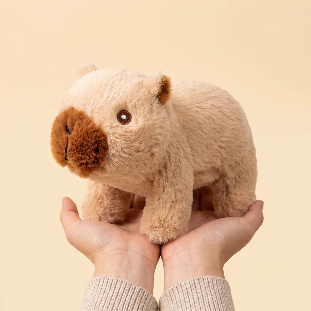 Brown walking capybara toy sitting in the cup of two joined palms, all four legs resting inside the hands